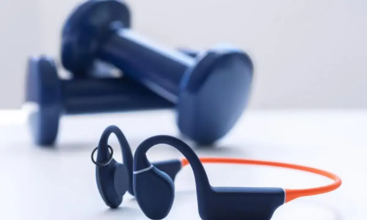 Un casque à conduction osseuse bleu et orange, prêt pour votre prochaine séance de sport, avec des haltères bleus en arrière-plan.