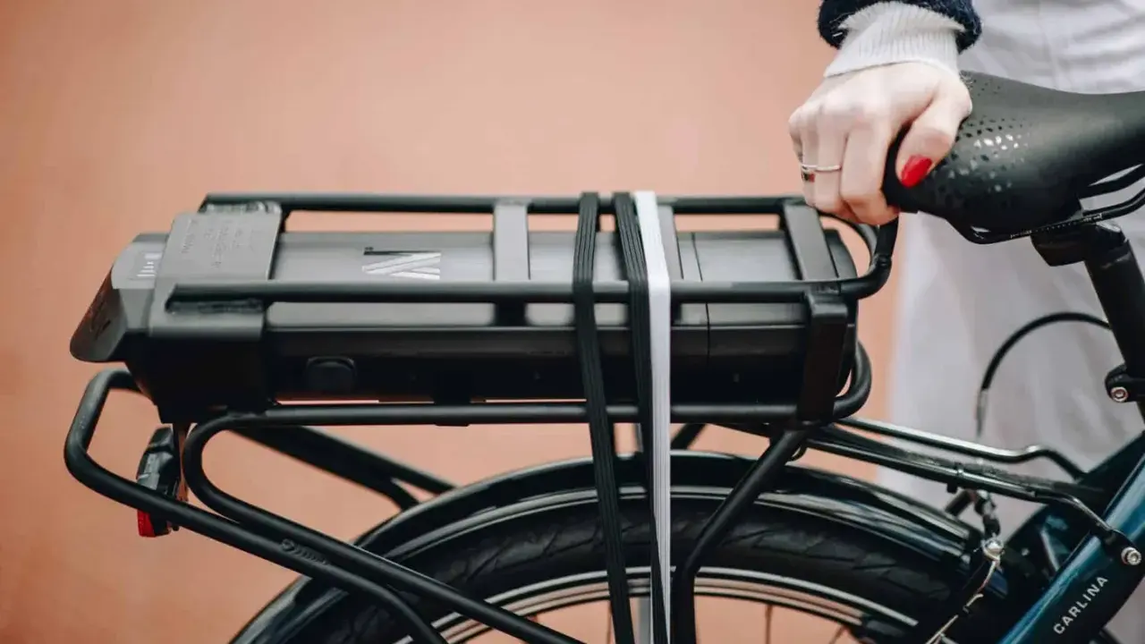 Main d'une femme tenant la selle d'un vélo électrique, avec la batterie visible sur le porte-bagages. Idéal pour tester la batterie du vélo.