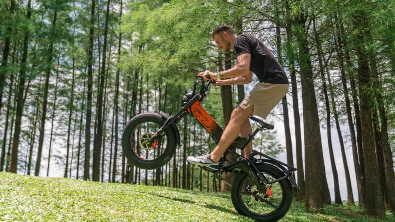 Un homme fait du vélo électrique en montée, le pneu avant décollé du sol. Il semble s'amuser, explorant quelle vitesse pour monter une côte en vélo électrique.