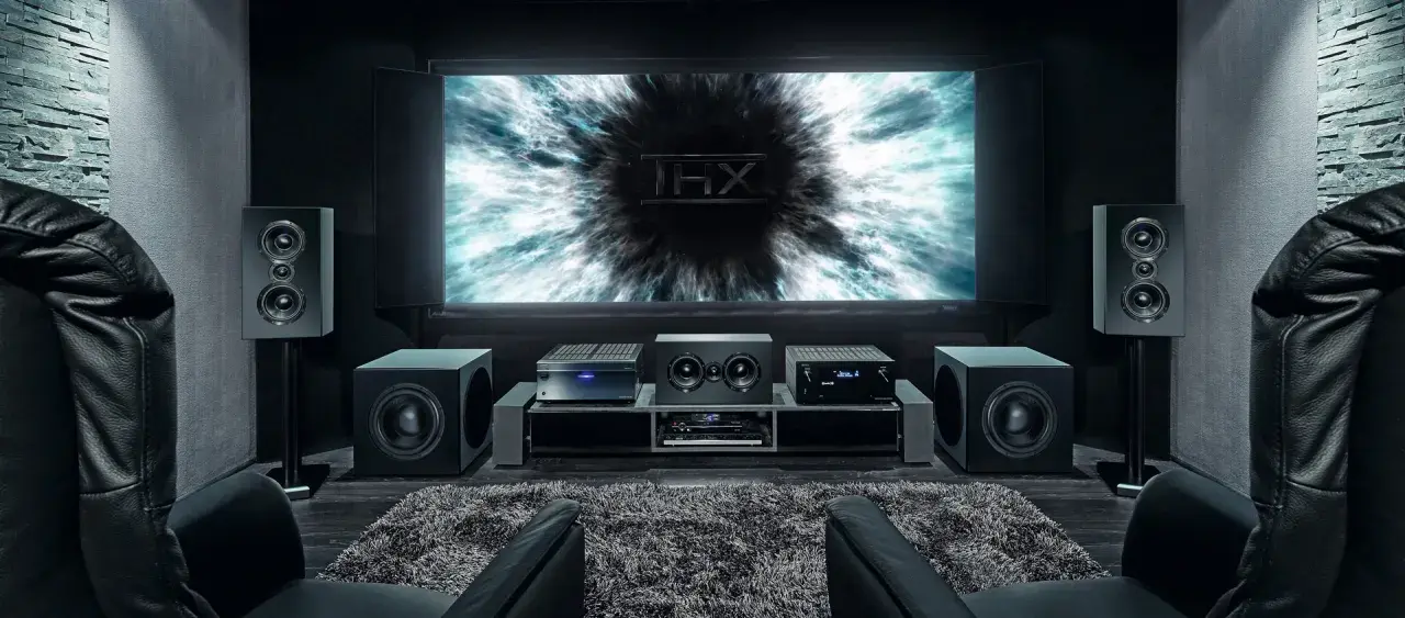 Installation home cinema avec écran THX, amplificateur, enceintes et fauteuils en cuir noir pour une expérience immersive.