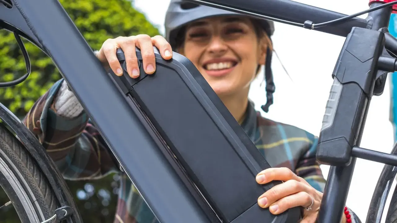 Une femme souriante manipule la batterie de son vélo électrique, peut-être pour apprendre comment réinitialiser une batterie de vélo électrique.