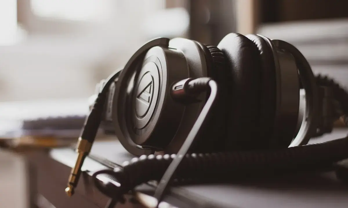 Gros plan sur un casque audio noir, avec son câble spiralé et sa prise jack dorée. La sensibilité du casque audio est palpable.