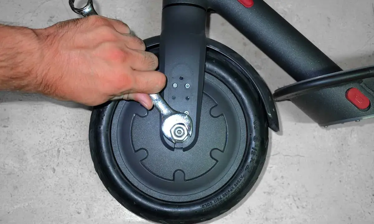 Main tenant utilise une clé pour changer la roue avant d'une trottinette électrique.