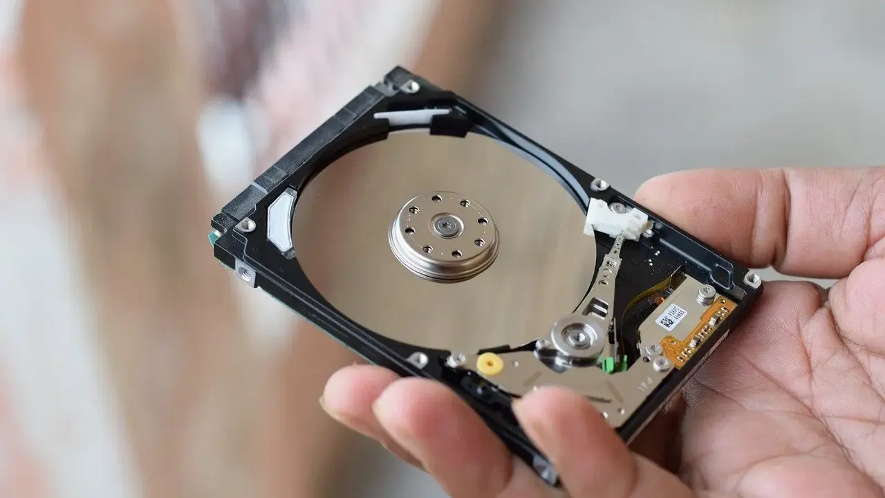 Main d'une personne tenant un disque dur interne, montrant les plateaux réfléchissants et les composants électroniques. Il existe différents types de disques durs.