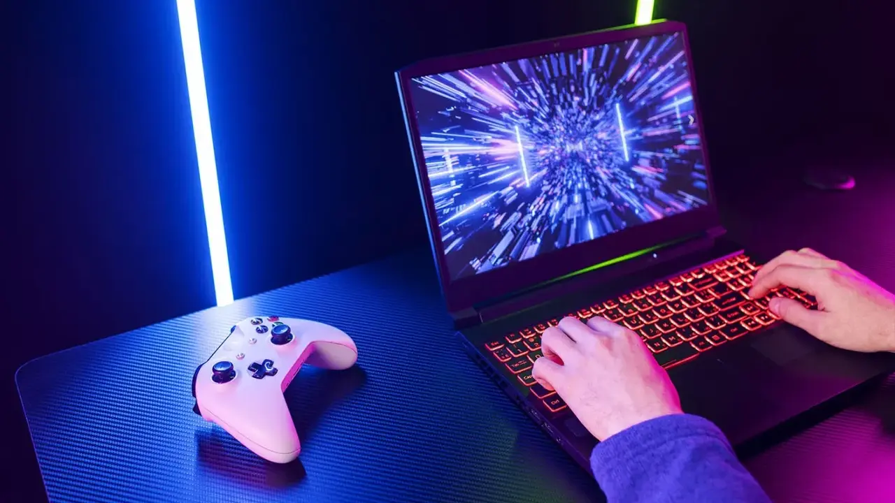 Un joueur utilise un PC portable gamer avec un clavier rétroéclairé. Une manette est posée à côté. Comment choisir son PC portable gamer ?