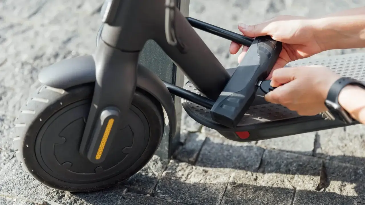 Mains tenant une clé pour comment attacher sa trottinette électrique. Le cadenas est fixé au cadre.