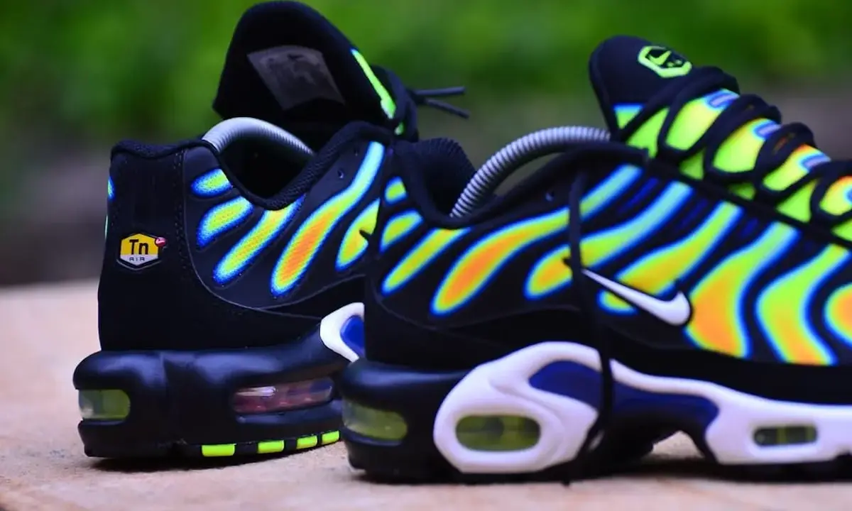 Paire de baskets Nike Air Max Plus TN, noires avec des vagues dégradées de jaune, orange et bleu.