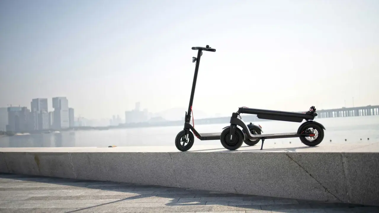 Une trottinette électrique s'allume mais ne bouge pas, posée sur un muret face à une ville et un pont.