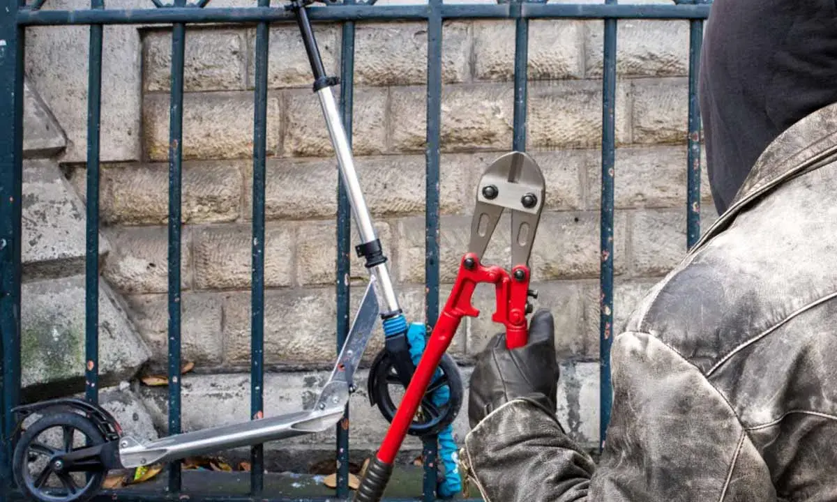 Un voleur, cagoulé et ganté, s'apprête à couper le cadenas d'une trottinette volée avec une pince monstre. Comment retrouver une trottinette volée ?