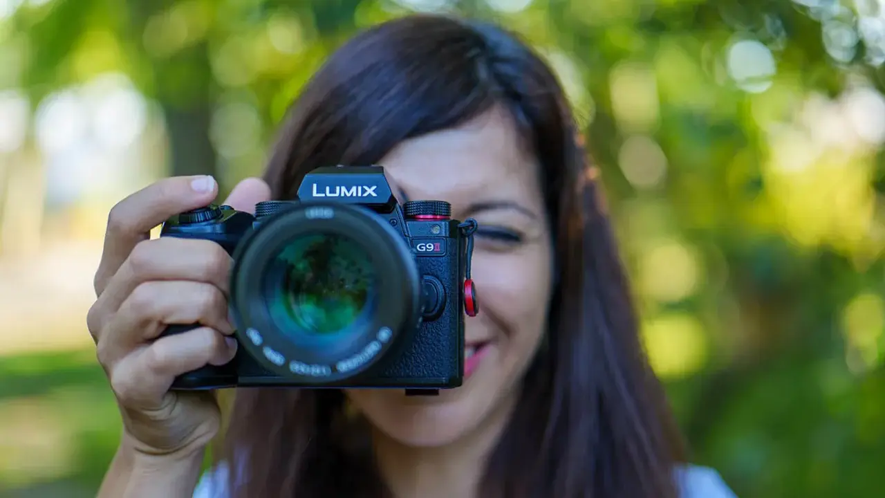 Une femme souriante tient un appareil photo Lumix G9II devant son visage. Un guide pour comment choisir son appareil photo.