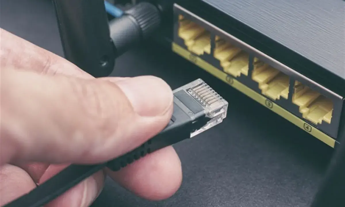 Maintenant, comment choisir son cable ethernet ? Une main tient un connecteur RJ45 près des ports d'un routeur.