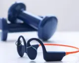 Un casque à conduction osseuse bleu et orange, prêt pour votre prochaine séance de sport, avec des haltères bleus en arrière-plan.