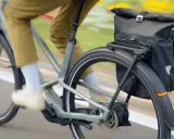 Un cycliste en pantalon kaki roule sur un vélo électrique gris, sacoche noire à l'arrière. Facile à utiliser, ce vélo offre une assistance douce.