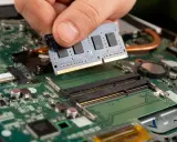 Main d'une personne installant un module de test RAM sur une carte mère d'ordinateur portable.