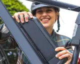 Une femme souriante manipule la batterie de son vélo électrique, peut-être pour apprendre comment réinitialiser une batterie de vélo électrique.