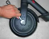 Main tenant utilise une clé pour changer la roue avant d'une trottinette électrique.