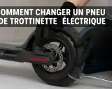 Mains gantées effectuant la réparation pneu trottinette électrique, démontant le pneu usé avec un levier.