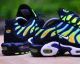 Paire de baskets Nike Air Max Plus TN, noires avec des vagues dégradées de jaune, orange et bleu.