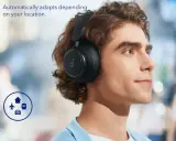 Un homme porte des écouteurs circum-auraux noirs qui s'adaptent automatiquement à son environnement, comme l'indiquent les icônes d'avion, de maison et de train.
