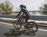 Un cycliste sur un vélo électrique qui se recharge en roulant, longeant une voie rapide bordée d'eau et d'arbres.