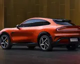 La **Xiaomi car** orange vif, un SUV coupé futuriste, se gare devant un bâtiment moderne aux reflets dorés.