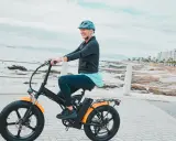 Une femme souriante roule sur un vélo électrique, profitant de la vue sur la mer. Le poid du vélo électrique ne l'empêche pas de profiter de sa balade.