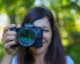 Une femme souriante tient un appareil photo Lumix G9II devant son visage. Un guide pour comment choisir son appareil photo.