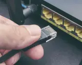 Maintenant, comment choisir son cable ethernet ? Une main tient un connecteur RJ45 près des ports d'un routeur.