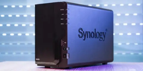 Un appareil Synology DS223, un nas stockage compact, est présenté sur un bureau en bois, avec un fond lumineux.