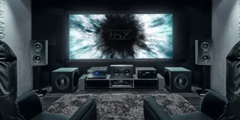 Installation home cinema avec écran THX, amplificateur, enceintes et fauteuils en cuir noir pour une expérience immersive.