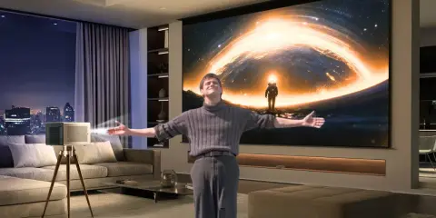 Un homme s'émerveille devant un vidéoprojecteur projetant une scène spatiale. Un guide pour comment choisir un vidéoprojecteur.