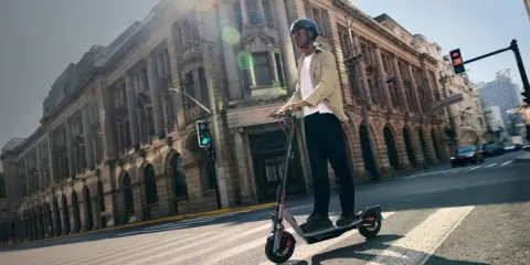 Un homme en casque roule sur la trottinette électrique la plus rapide du monde, traversant une rue bordée de bâtiments historiques.