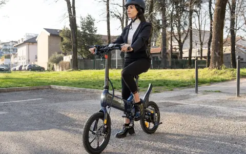 Femme en costume, casque, assise sur une trottinette Urban Glide qui n'avance plus. Elle semble dépitée.