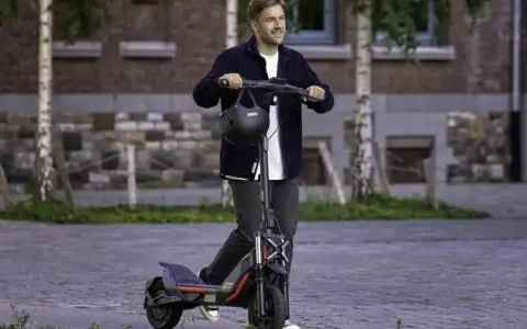 Un homme souriant sur une trottinette électrique puissante, dépassant les 25 km/h. La réglementation sur ces engins est à considérer.