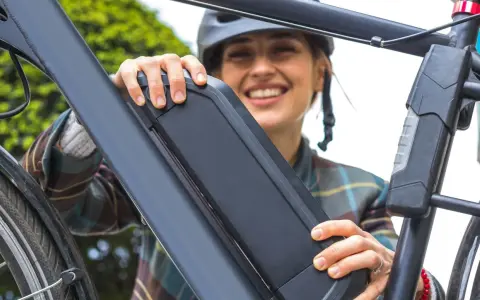 Une femme souriante manipule la batterie de son vélo électrique, peut-être pour apprendre comment réinitialiser une batterie de vélo électrique.
