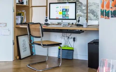 Bureau moderne avec iMac, chaise en rotin et étagères. Idéal pour savoir comment choisir un ordinateur de bureau adapté à votre espace de travail.