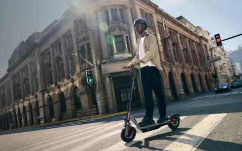 Un homme roule en trottinette électrique dans une rue bordée de bâtiments anciens. La taille roue trottinette semble adaptée à la ville.