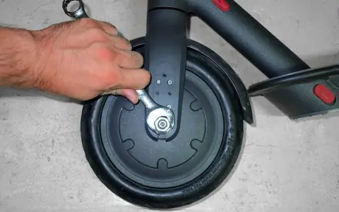 Main tenant utilise une clé pour changer la roue avant d'une trottinette électrique.