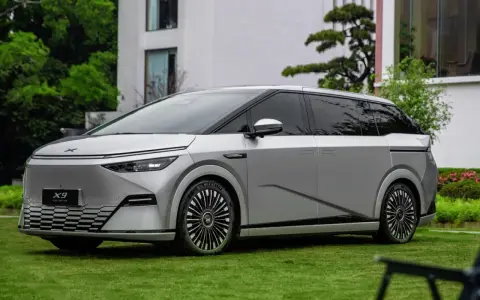Le Xpeng X9, un monospace argenté futuriste, est garé sur une pelouse verte devant un bâtiment moderne.