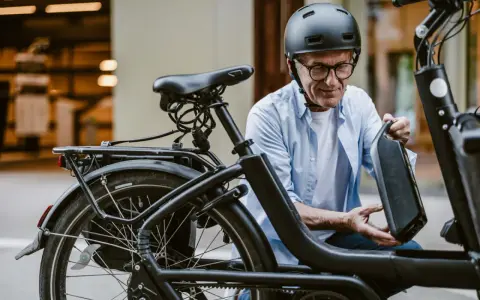 Un homme en casque retire la batterie de son vélo électrique, prêt pour l'immatriculation vélo électrique.