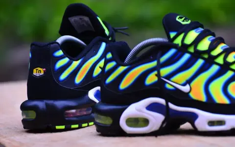Paire de baskets Nike Air Max Plus TN, noires avec des vagues dégradées de jaune, orange et bleu.