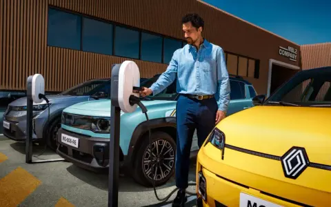Un homme charge une automobile hybride électrique turquoise. Une voiture jaune est garée à côté.