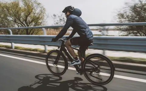 Un cycliste sur un vélo électrique qui se recharge en roulant, longeant une voie rapide bordée d'eau et d'arbres.