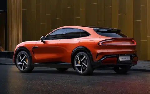 La **Xiaomi car** orange vif, un SUV coupé futuriste, se gare devant un bâtiment moderne aux reflets dorés.