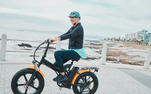 Une femme souriante roule sur un vélo électrique, profitant de la vue sur la mer. Le poid du vélo électrique ne l'empêche pas de profiter de sa balade.