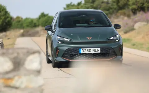 La Cupra Born VZ, d'un vert profond, roule sur une route de campagne. Un conducteur porte des lunettes de soleil.