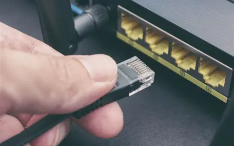 Maintenant, comment choisir son cable ethernet ? Une main tient un connecteur RJ45 près des ports d'un routeur.