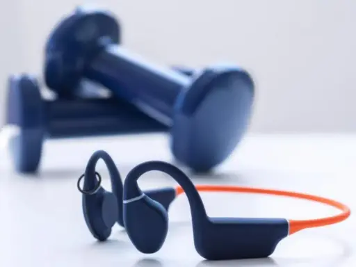 Un casque à conduction osseuse bleu et orange, prêt pour votre prochaine séance de sport, avec des haltères bleus en arrière-plan.