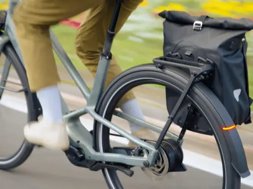 Un cycliste en pantalon kaki roule sur un vélo électrique gris, sacoche noire à l'arrière. Facile à utiliser, ce vélo offre une assistance douce.