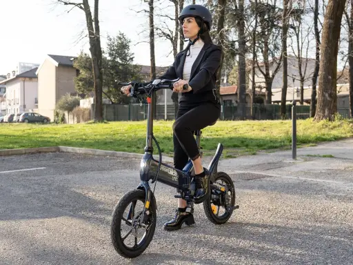 Femme en costume, casque, assise sur une trottinette Urban Glide qui n'avance plus. Elle semble dépitée.